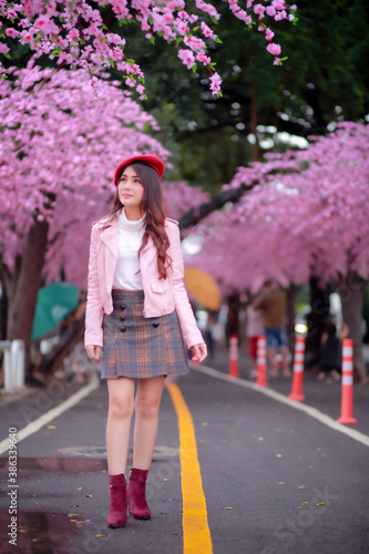 A traveler hipster woman sightseeing wear a red hat and a smooth leather dress with beautiful sakura cherry blossoms tree full blooming in pink color in the park on a spring day. © Narin Sapaisarn