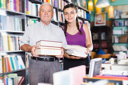 Glad old man with granddaughter are showing their purchases in bookstore