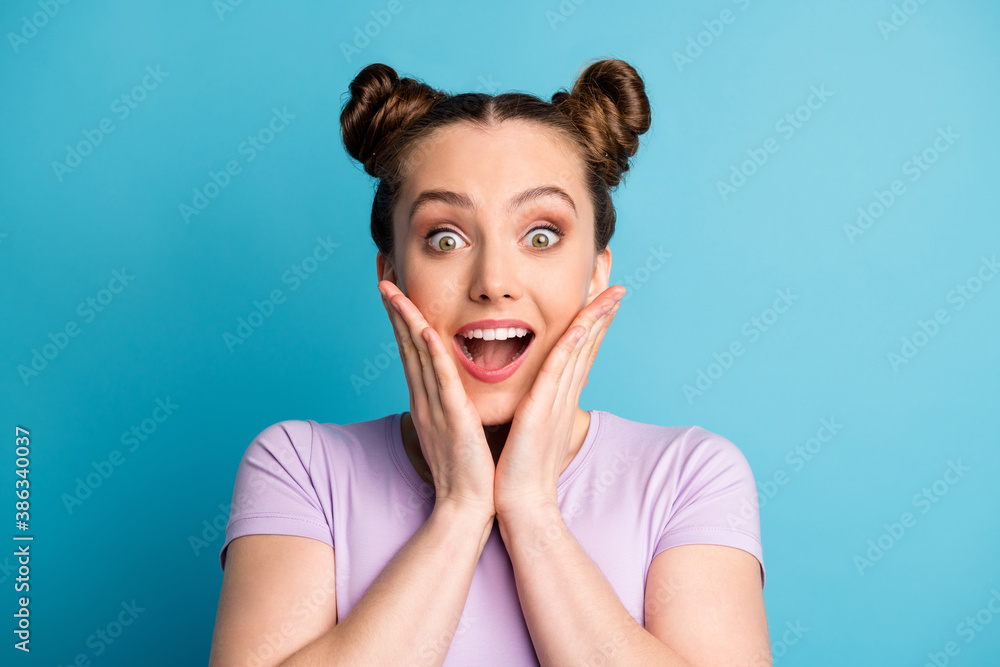 Photo of attractive shocked crazy teen lady two funny pretty buns good mood excited expression listen unexpected news arms on cheeks wear casual purple t-shirt isolated blue color background Photo of attractive shocked crazy teen lady two funny pretty buns good mood excited expression listen unexpected news arms on cheeks wear casual purple t-shirt isolated blue color background