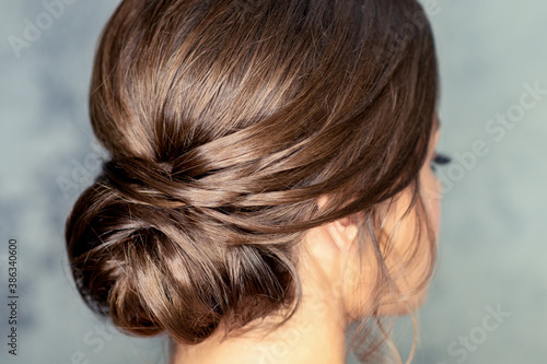 Rear view of young brunette woman with beautiful middle bun hairstyle on gray background