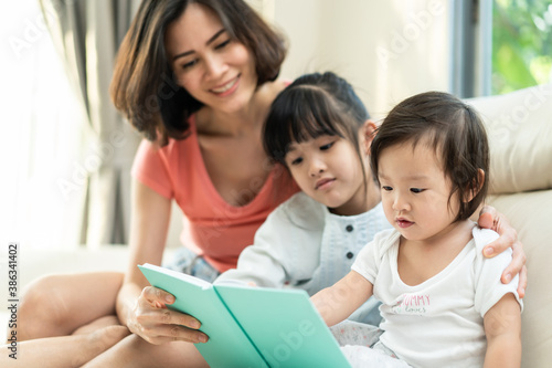 Asian young mother holding book to their daughter for drawing together