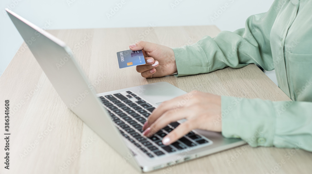 The businesswoman's hand is holding a credit card and using a laptop for online shopping and internet payment in the office The businesswoman's hand is holding a credit card and using a laptop for online shopping and internet payment in the office