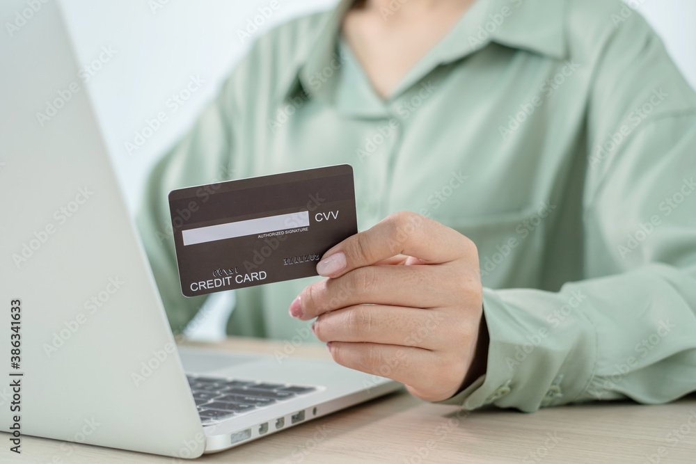 The businesswoman's hand is holding a credit card and using a laptop for online shopping and internet payment in the office The businesswoman's hand is holding a credit card and using a laptop for online shopping and internet payment in the office