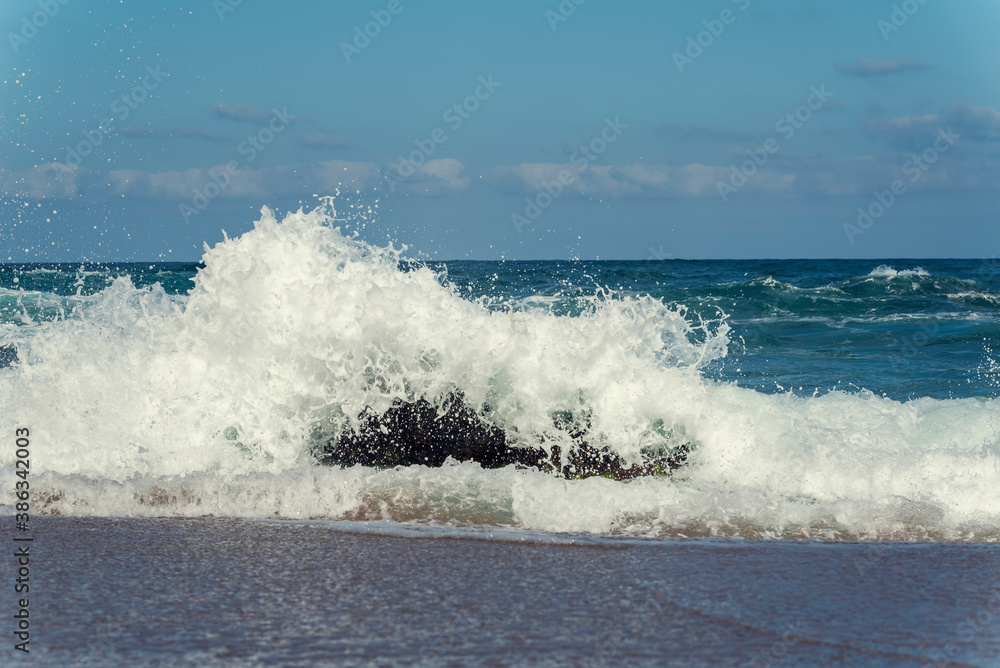 Fototapeta premium Waves crashing into a rock in the sea with power and making white foam Selective focus