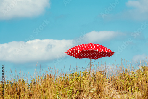 One red parasol with white dots in a green and dry grass on a sand beach Selective focus