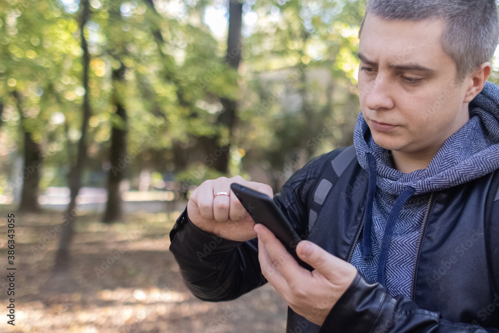 A man in a leather jacket looks at the phone in the middle of the forest. Social media immersion, orienteering, and phone stress concept A man in a leather jacket looks at the phone in the middle of the forest. Social media immersion, orienteering, and phone stress concept