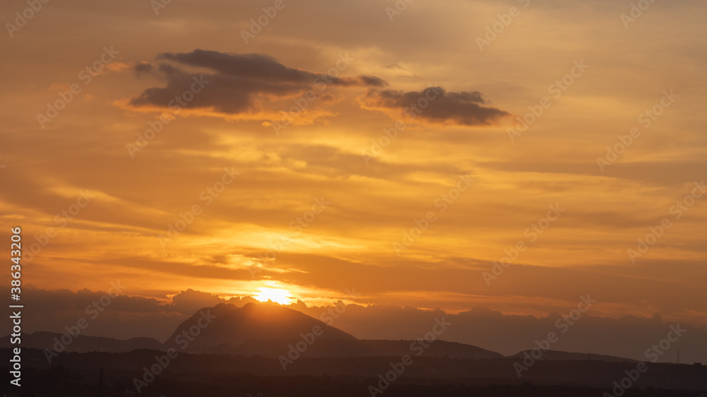 Silhouette of a hill against beautiful golden hour light and beautiful clouds formation in the horizon with the sun setting 