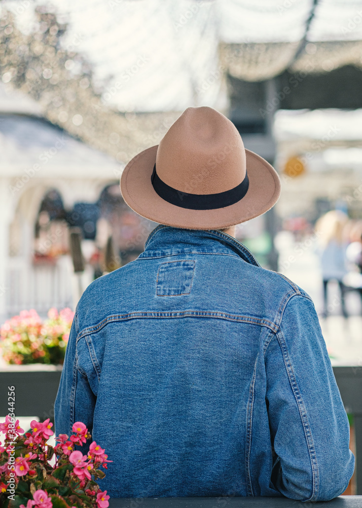 A man in a denim jacket and a hat stands with his back and looks at the busy street. Tourism concept, summer vacation.