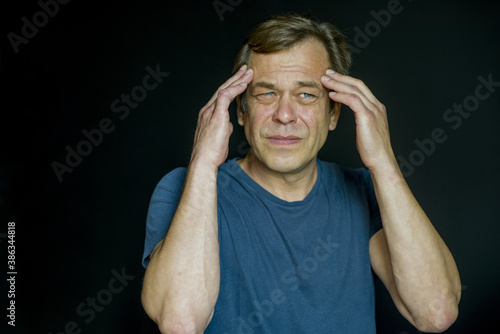 Foto Portrait of a 45-50-year-old man holding his head in his hands on a dark background