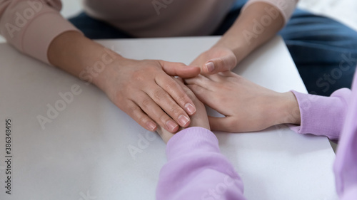 Crop close up top view of supportive Caucasian mother parent hold touch unhappy teen daughter hands show love and care. Mom parent caress comfort support sad unhappy teenage child. Parenthood concept.