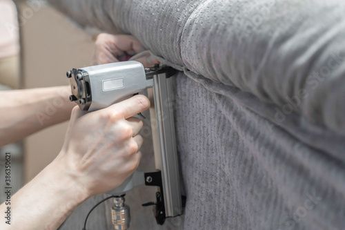 worker with tool changes sofa upholstery, close up blurred background