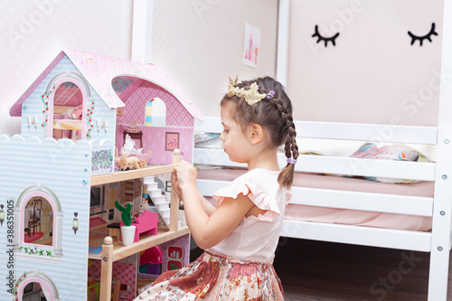 Beautiful little girl in pink dress plays with a doll's house