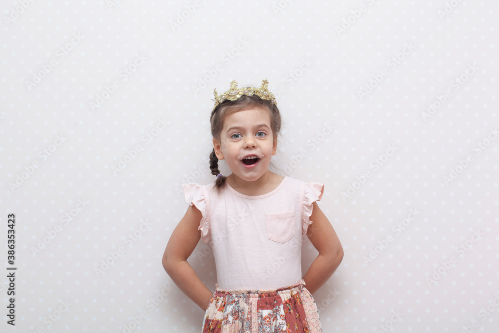 Surprised pretty young girl in pink dress with crown on head expressing isolated on pink background. Copy space for your text