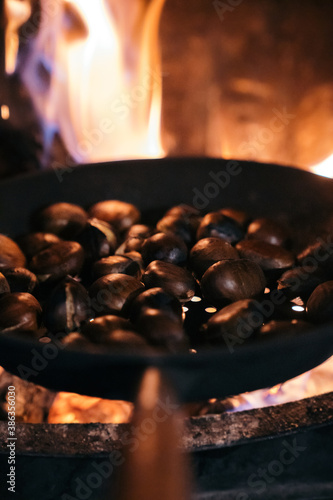 Roasted chestnuts in a frying pan on the fireplace. Cooking chestnuts in the fireplace with firewood and flames.