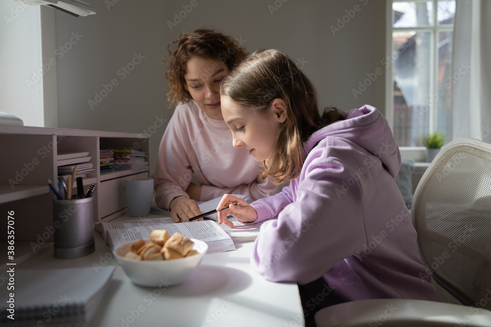 Smart teenage girl read textbook learning studying with caring mother. Focused 12s teenager pupil do prepare school homework task assignment with loving mom helping. Distant education concept. Smart teenage girl read textbook learning studying with caring mother. Focused 12s teenager pupil do prepare school homework task assignment with loving mom helping. Distant education concept.