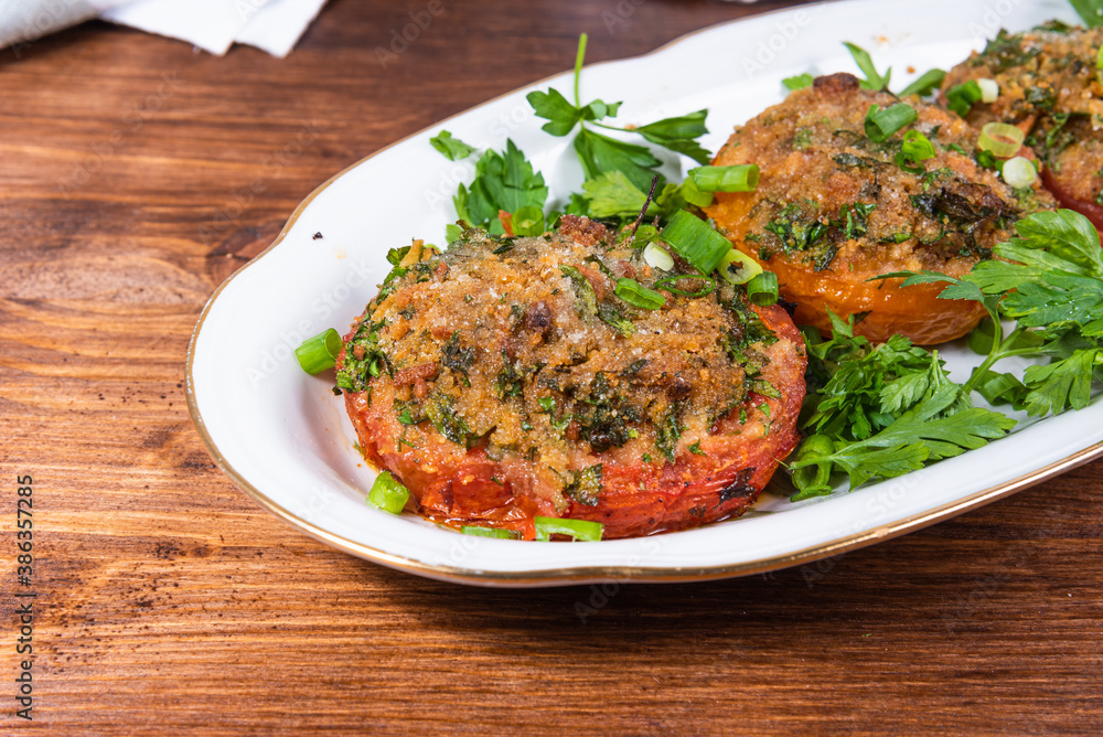 Provencal tomatoes - baked tomato halves with breadcrumbs and herbs on an oval dish, rustic background