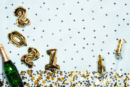 Champagne bottle and 2021 balloons with black and gold stars and circle confetti on the blue background. Christmas or New Year festive concept. Top view and flat lay.