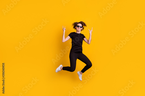 Full length body size view of attractive cool naughty playful cheery girl jumping showing horn symbol isolated bright yellow color background