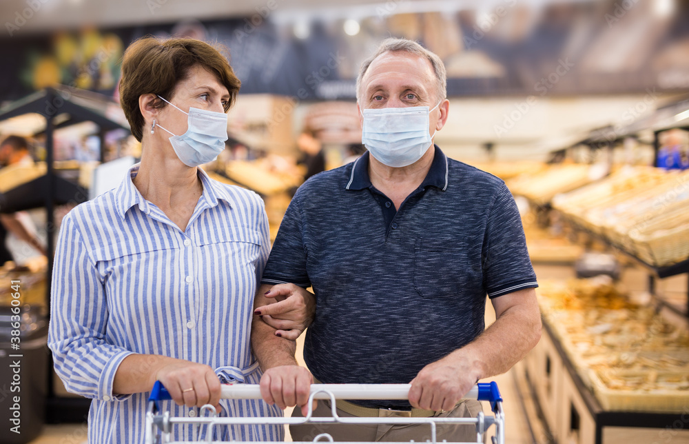Elderly married couple wearing protective masks buying food and pastries in mall