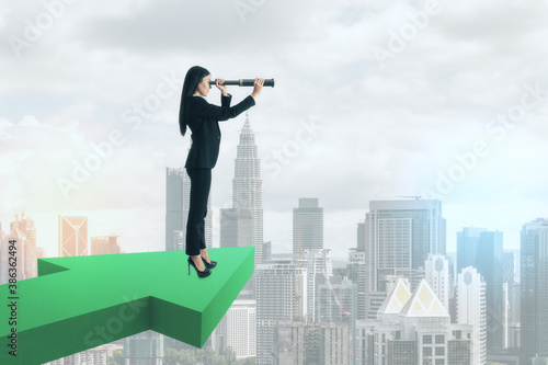 Businesswoman with spyglass standing on green arrow photo