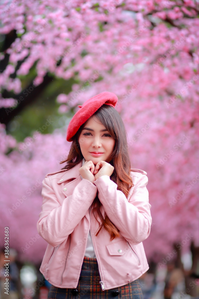 A traveler hipster woman sightseeing wear a red hat and a smooth leather dress with beautiful sakura cherry blossoms tree full blooming in pink color in the park on a spring day. A traveler hipster woman sightseeing wear a red hat and a smooth leather dress with beautiful sakura cherry blossoms tree full blooming in pink color in the park on a spring day.
