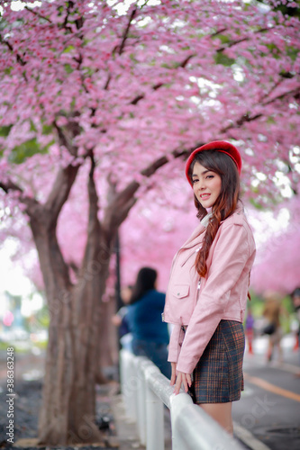 A traveler hipster woman sightseeing wear a red hat and a smooth leather dress with beautiful sakura cherry blossoms tree full blooming in pink color in the park on a spring day.