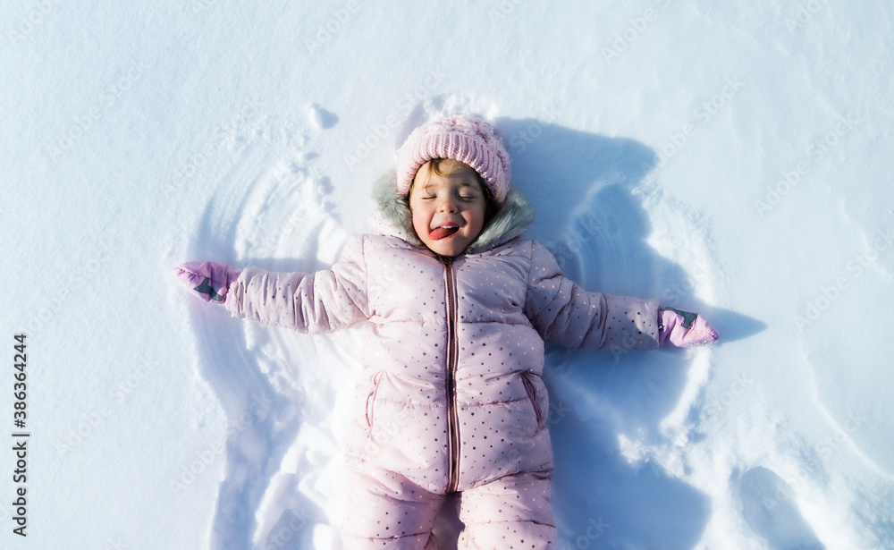 Top view portrait of cheerful small girl lying in snow in winter nature, making angels. Top view portrait of cheerful small girl lying in snow in winter nature, making angels.