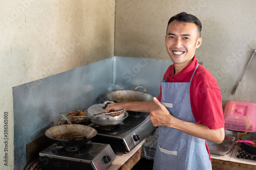 the male waiter smiles with a thumbs up while frying side dishes for customers at the stall photo