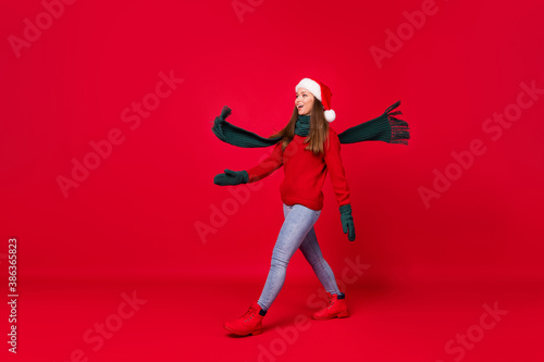 Full length body size profile side view of her she nice attractive cheerful cheery glad girl wearing festal cap walking wind blowing scarf isolated over bright vivid shine vibrant red color background