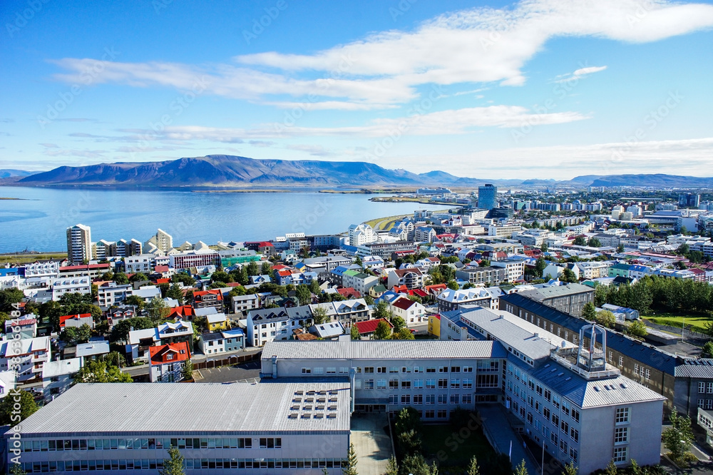Colored roofs of houses in Rekjavik against the background of blue sky and a large mountain. Iceland - obrazy, fototapety, plakaty 