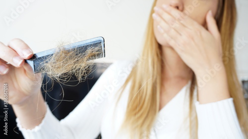 Young blond woman is shocked because of hair loss while holding a hairy comb