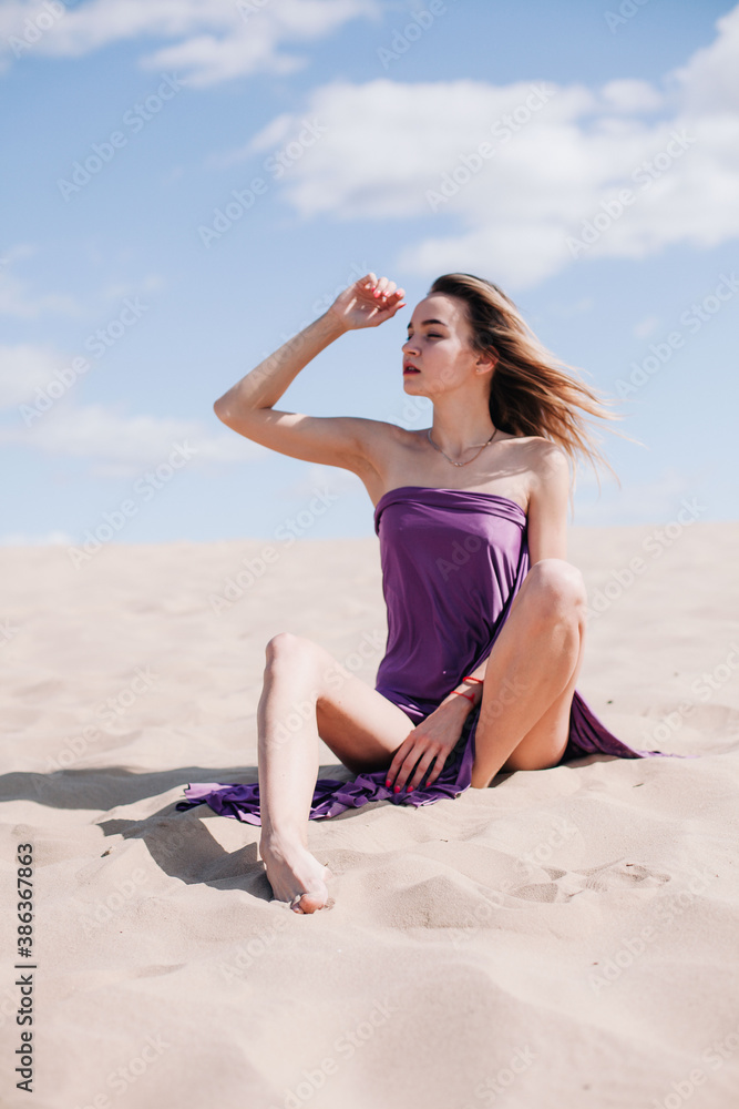 A young, slender girl in a beige dress with purple cloth in her hands posing in the desert in the wind A young, slender girl in a beige dress with purple cloth in her hands posing in the desert in the wind