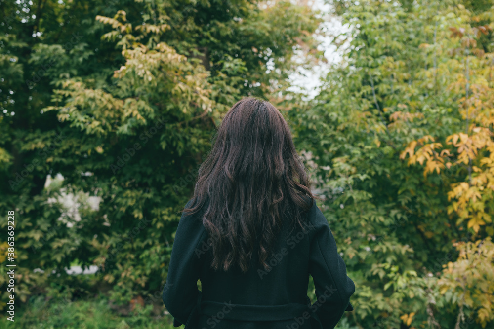 Portait from the back of female in dark coat outdoors in park or forest Portait from the back of female in dark coat outdoors in park or forest