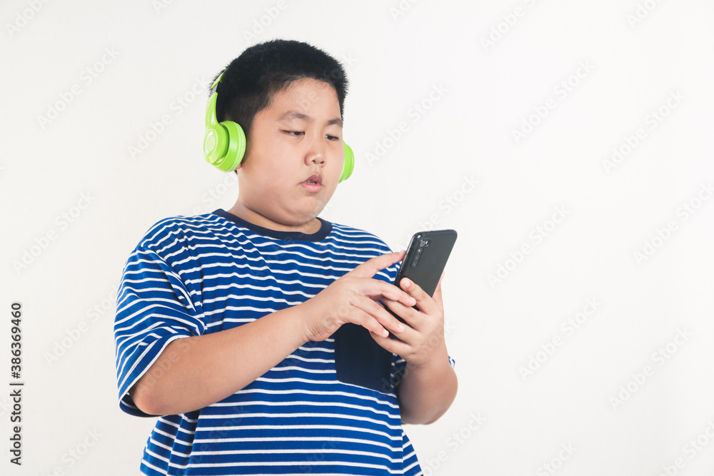 Asian fat boy standing playing smartphone Wearing headphones to music watching him happy. white background Asian fat boy standing playing smartphone Wearing headphones to music watching him happy. white background