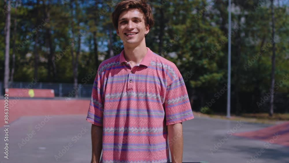Smiling cute young charismatic guy in front of the camera in a modern skate park he have a great mood looking straight to the camera Smiling cute young charismatic guy in front of the camera in a modern skate park he have a great mood looking straight to the camera