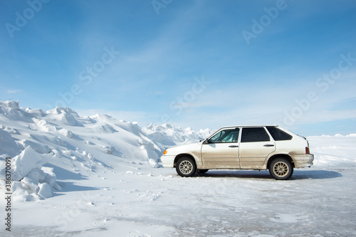 Side view of a car standing by a huge snowdrift formed after cleaning roads. The concept of cleaning roads from snow