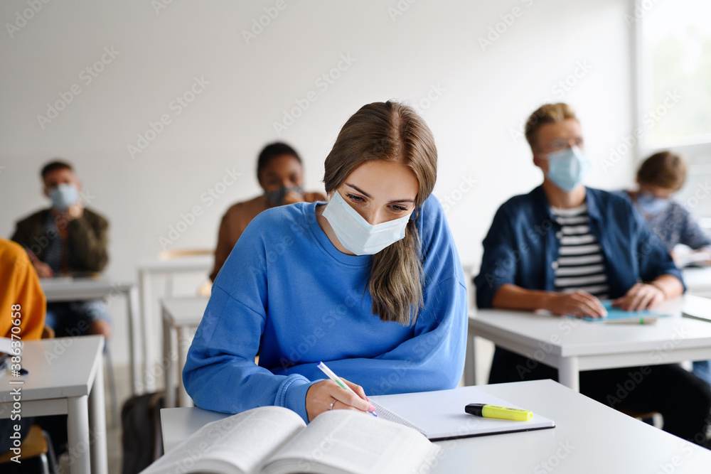 Young students with face masks at desks at college or university, coronavirus concept. - obrazy, fototapety, plakaty 