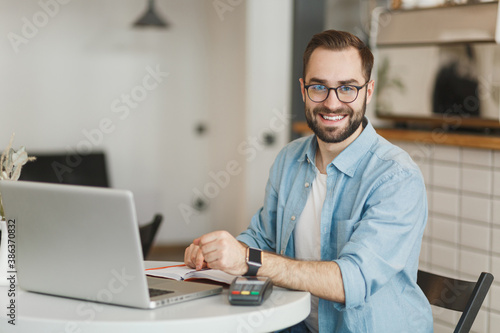 Handsome man in glasses sit at table in coffee shop cafe restaurant indoor working studying on laptop computer pay off with smart watch bank payment terminal. Freelance mobile office business concept.