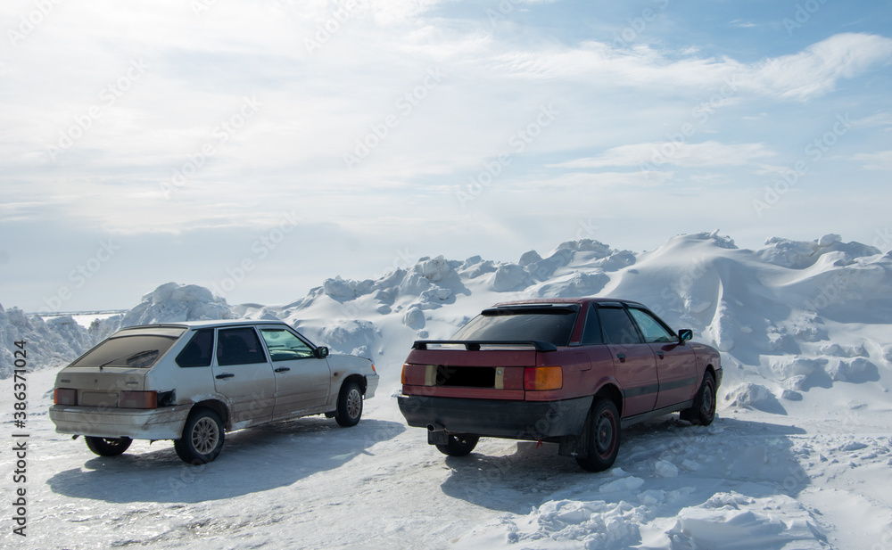 Rear view of cars standing by a huge snowdrift formed after clearing the roads from snow