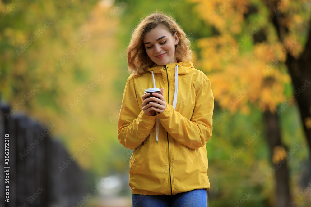 Woman in yellow jacket drinks a tea walking along fall alley Woman in yellow jacket drinks a tea walking along fall alley