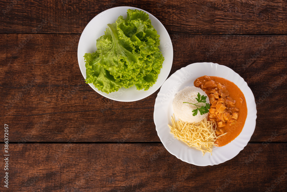 Rice, chicken stroganoff, potato straw and lettuce in white dish, on wooden surface, gray background, top view. Rice, chicken stroganoff, potato straw and lettuce in white dish, on wooden surface, gray background, top view.