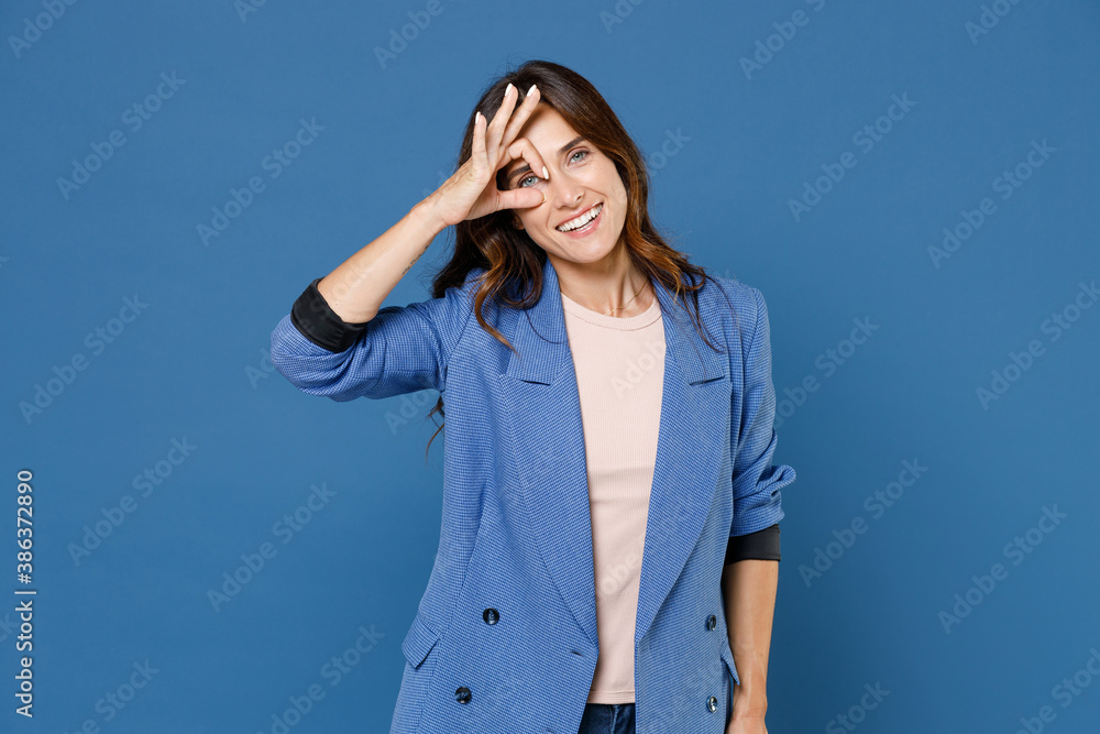 Smiling cheerful laughing funny pretty young brunette woman 20s wearing basic jacket hold hands near eyes, imitating glasses or binoculars isolated on bright blue colour background, studio portrait. Smiling cheerful laughing funny pretty young brunette woman 20s wearing basic jacket hold hands near eyes, imitating glasses or binoculars isolated on bright blue colour background, studio portrait.