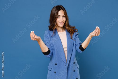 Fotografie Smiling young brunette woman 20s wearing basic jacket standing rubbing fingers showing cash gesture asking for money looking camera isolated on bright blue colour wall background studio portrait