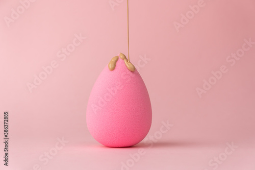 The foundation flows down the sponge for applying makeup in the form of a drop or egg, on a delicate pink background photo