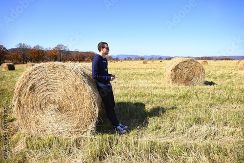Young brunette man in warm jacket leaning against haystack in field with bales of hay. he looking to the right. Primorsky kray, Russia. Beauty in nature. Copy space
