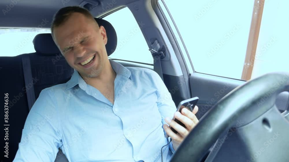 portrait of a young man who uses a smartphone while driving a car and laughs. portrait of a young man who uses a smartphone while driving a car and laughs.