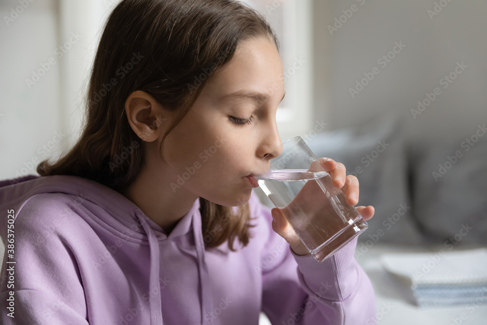 Thirsty small 12s Caucasian teen girl drink pure mineral clean water from glass for body refreshment. Little teenager child kid feel dehydrated enjoy aqua at home. Hydration, healthy habit concept.