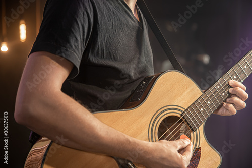 The guitarist plays an acoustic guitar in concert with a pick on a black blurred background.