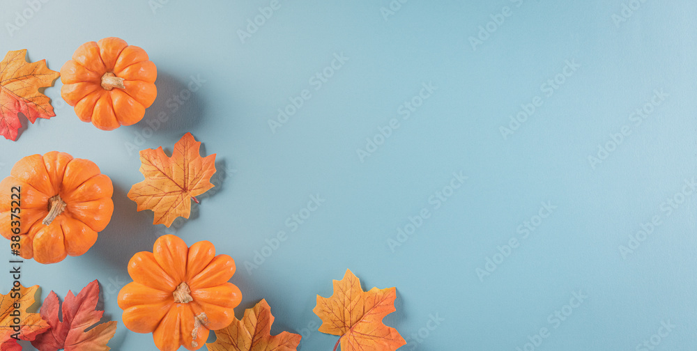 Thanksgiving background decoration from dry leaves and pumpkin on  pastel blue background. Flat lay, top view with copy space.