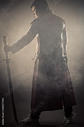 person in jacket with sword standing back in smoke